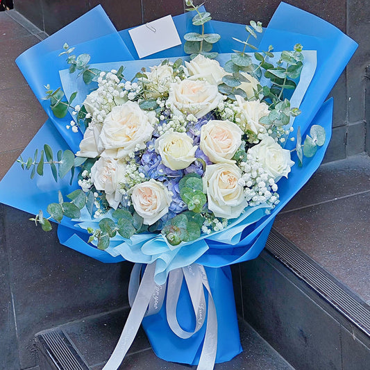 ช่อดอกกุหลาบสายพันธุ์อังกฤษ สีขาว 15 ดอก และ ไฮเดรนเยียสีฟ้า และ ใบไม้แซม ห่อกระดาษสีน้ำเงินฟ้า