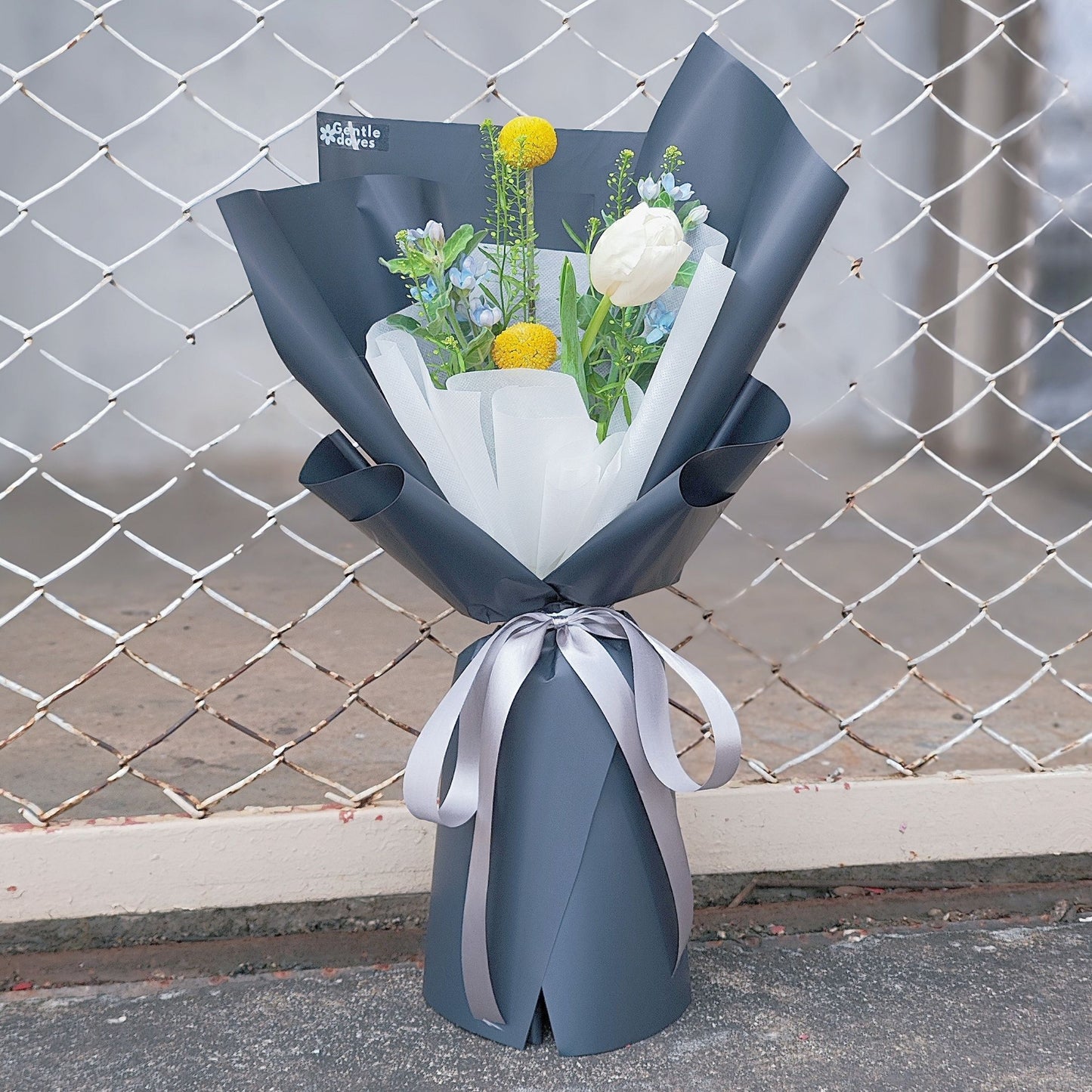 Single White Tulip with Premium Filler Flowers in Dark Blue Paper Bouquet