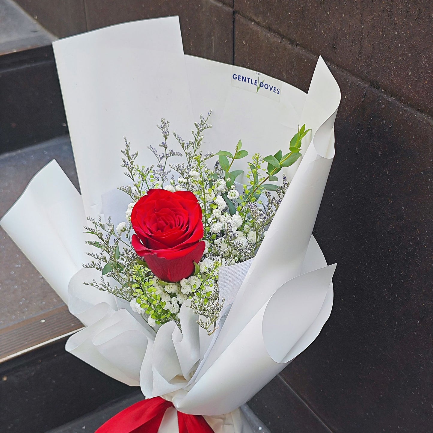 Single Imported Red Rose with Green Foliage in White Paper Bouquet