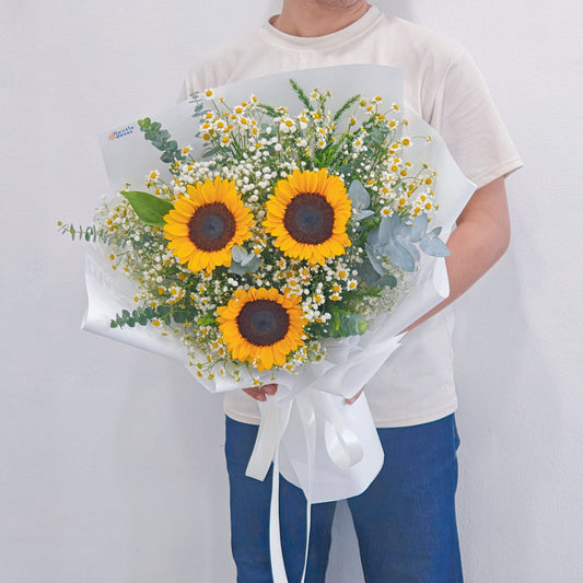Three Sunflowers with Daisies and Foliage in White Paper Bouquet.