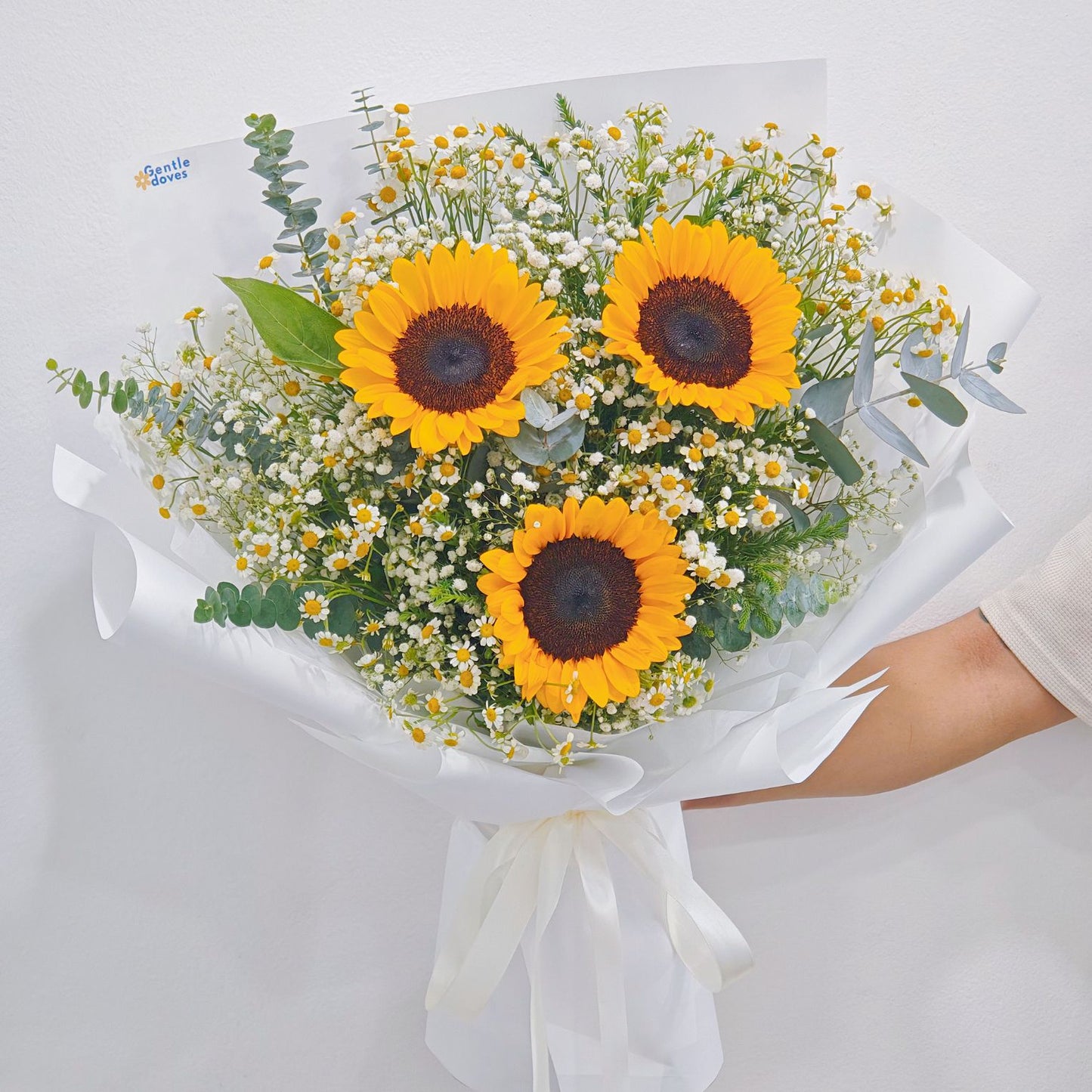 Three Sunflowers with Daisies and Foliage in White Paper Bouquet.