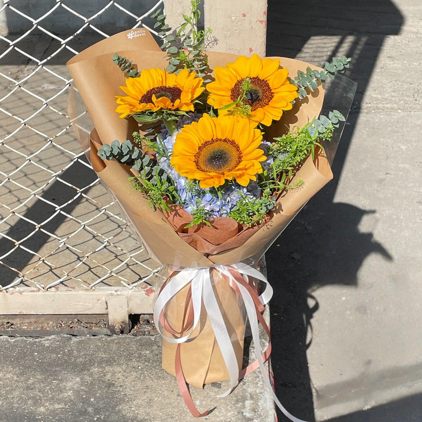 Three Sunflowers with Blue Hydrangeas and Green Foliage in Kraft Paper Bouquet