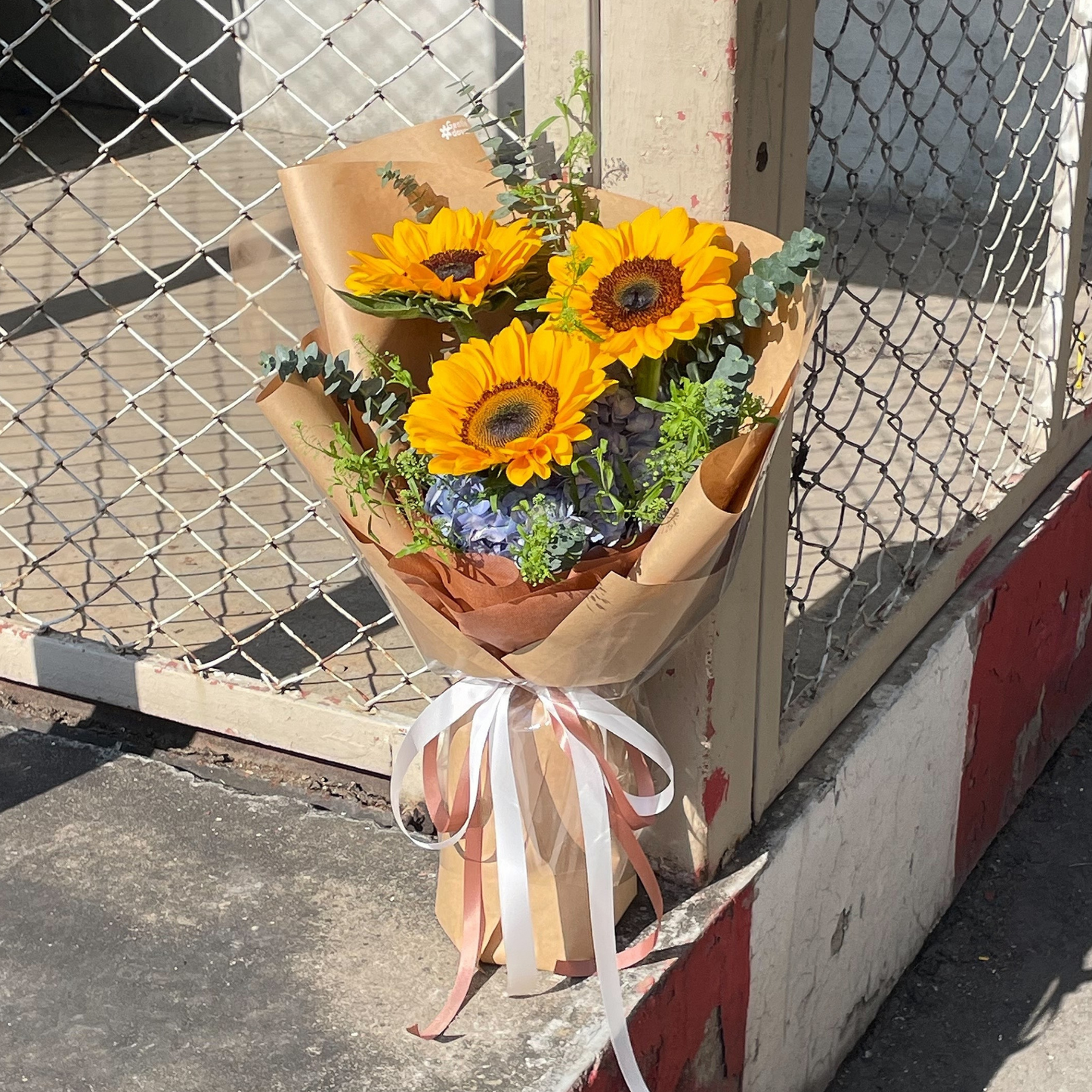 Three Sunflowers with Blue Hydrangeas and Green Foliage in Kraft Paper Bouquet