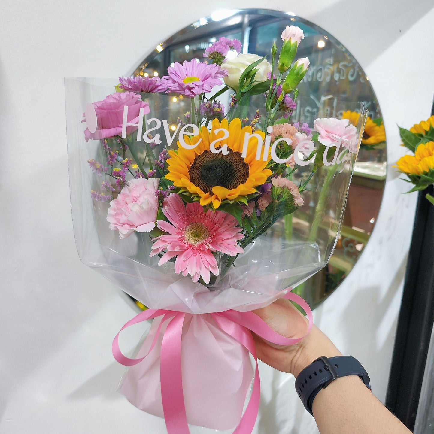 ช่อดอกไม้คละ โทนสีชมพู มีข้อความติด 'Have a Nice Day' และทานตะวัน