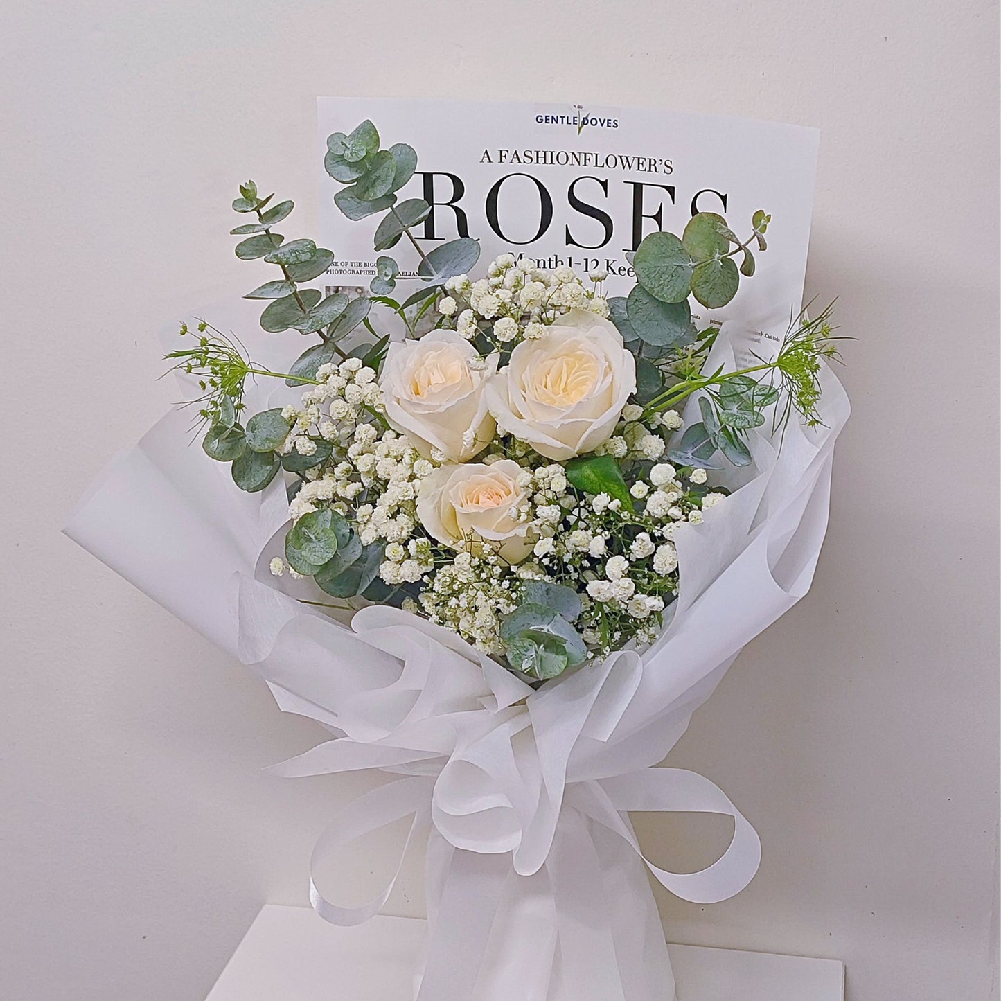 Three White English Roses with Gypsophila and Green Foliage in All White Paper Bouquet