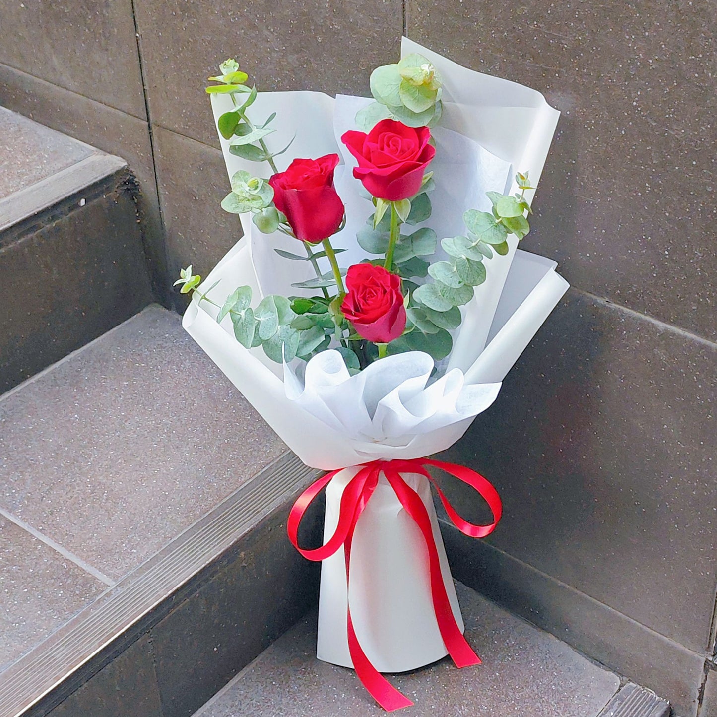 Three Imported Red Roses with Eucalyptus in White Paper Bouquet