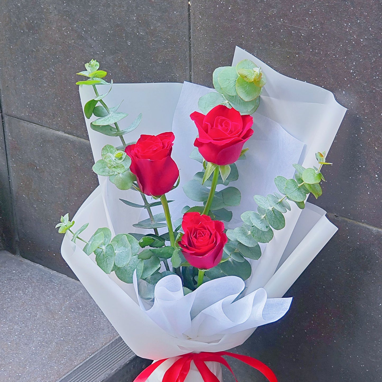 Three Imported Red Roses with Eucalyptus in White Paper Bouquet