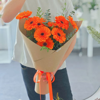 Nine Vivid Orange Gerberas with Green Foliage in Kraft Paper Bouquet