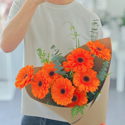 Nine Vivid Orange Gerberas with Green Foliage in Kraft Paper Bouquet