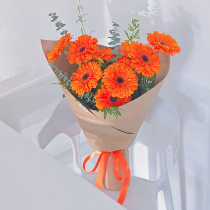 Nine Vivid Orange Gerberas with Green Foliage in Kraft Paper Bouquet