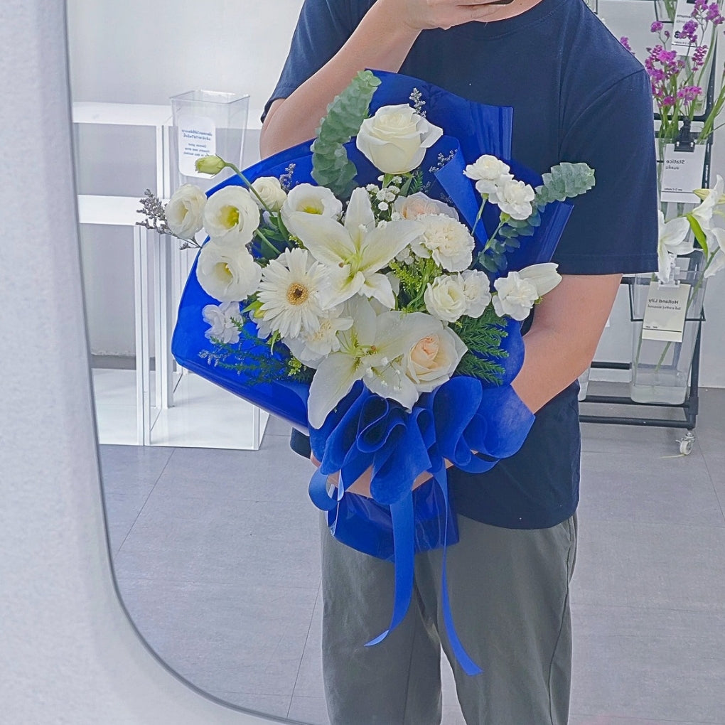 ช่อดอกไม้คละ โทนสีขาว และ ดอกลิลลี่ กับ ใบไม้แซมโทนสีเขียว ห่อกระดาษสีนำเงิน